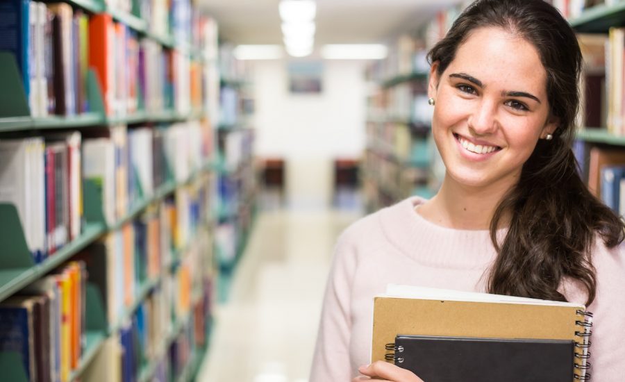 In the library - pretty female student with books working in a high school library.