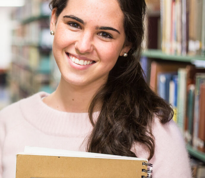 In the library - pretty female student with books working in a high school library.